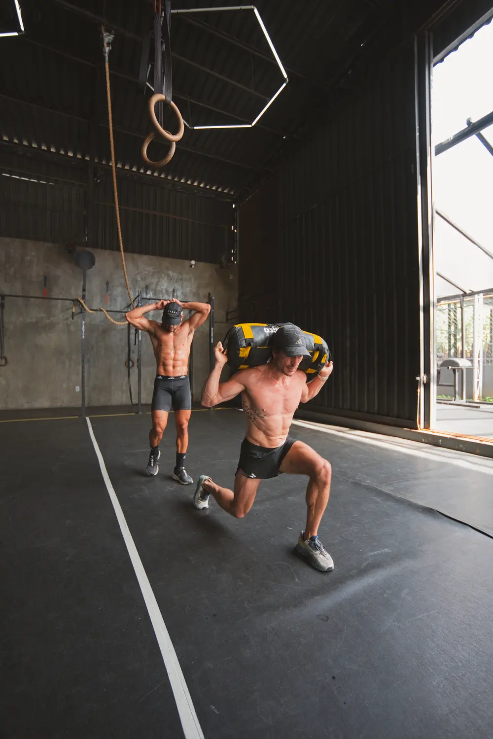 Dupla fazendo sandbag lunges no simulado HYROX da Crown Clube Fla